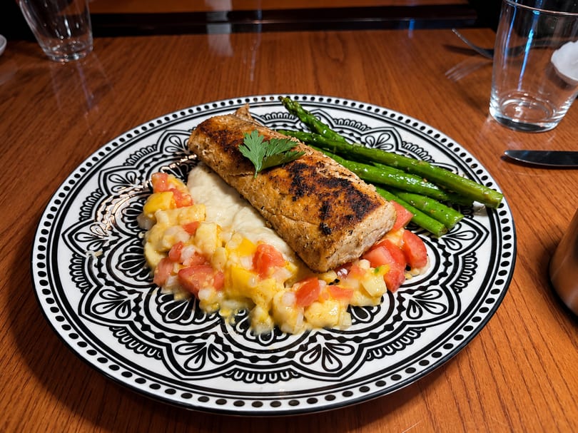 Grilled fish with asparagus, mashed potatoes, and tomato salsa on a decorative plate.