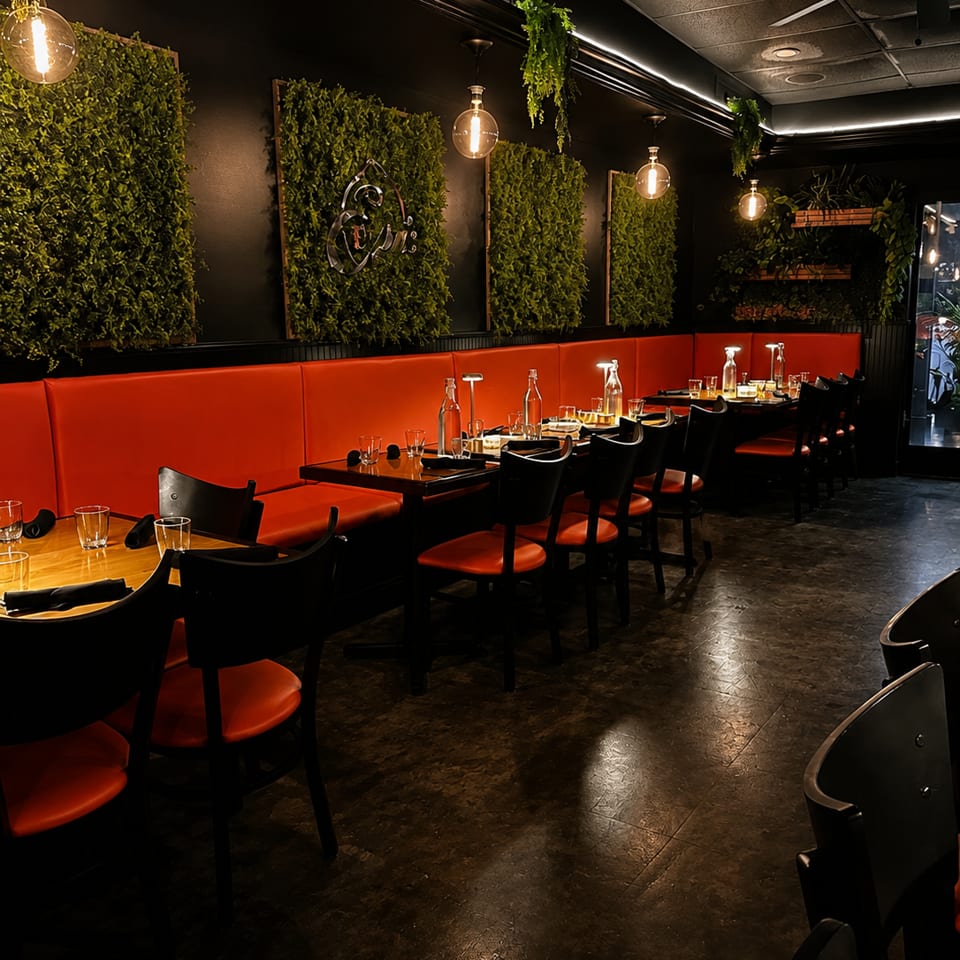 Modern restaurant interior with orange booths, dark tables, green wall panels, and Edison bulb lighting.