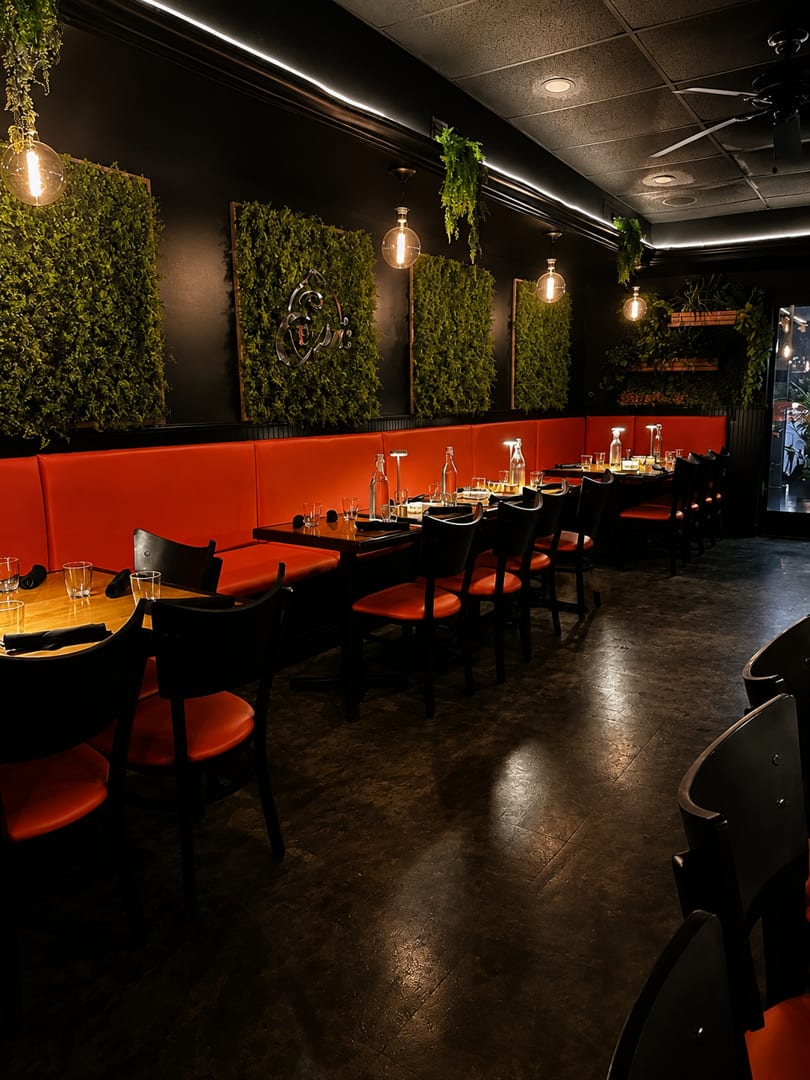 Modern restaurant interior with orange booths, dark tables, green wall panels, and Edison bulb lighting.