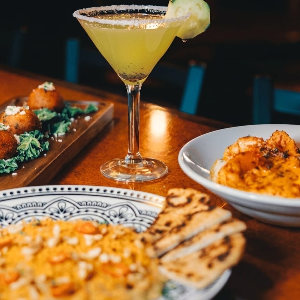 A table spread with a cocktail, fried appetizers, shrimp and grits, and a rice dish.