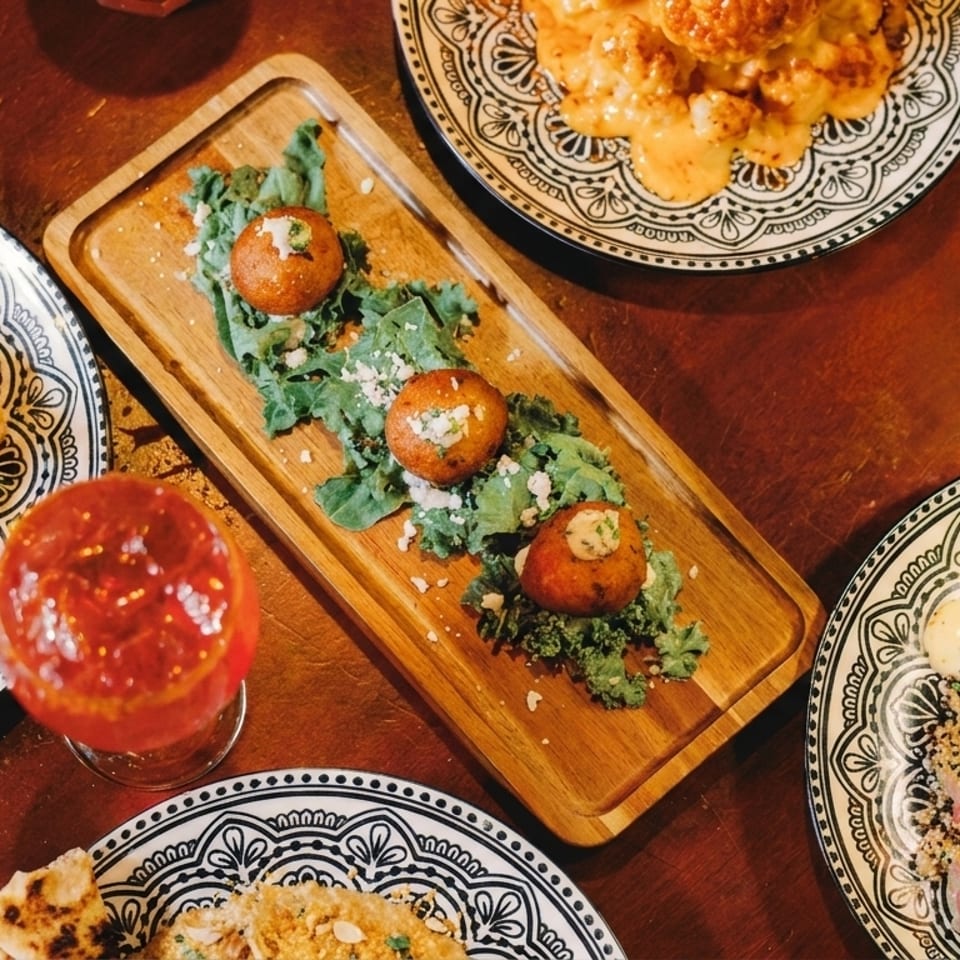 Overhead view of various dishes and cocktails on a dark wooden table.