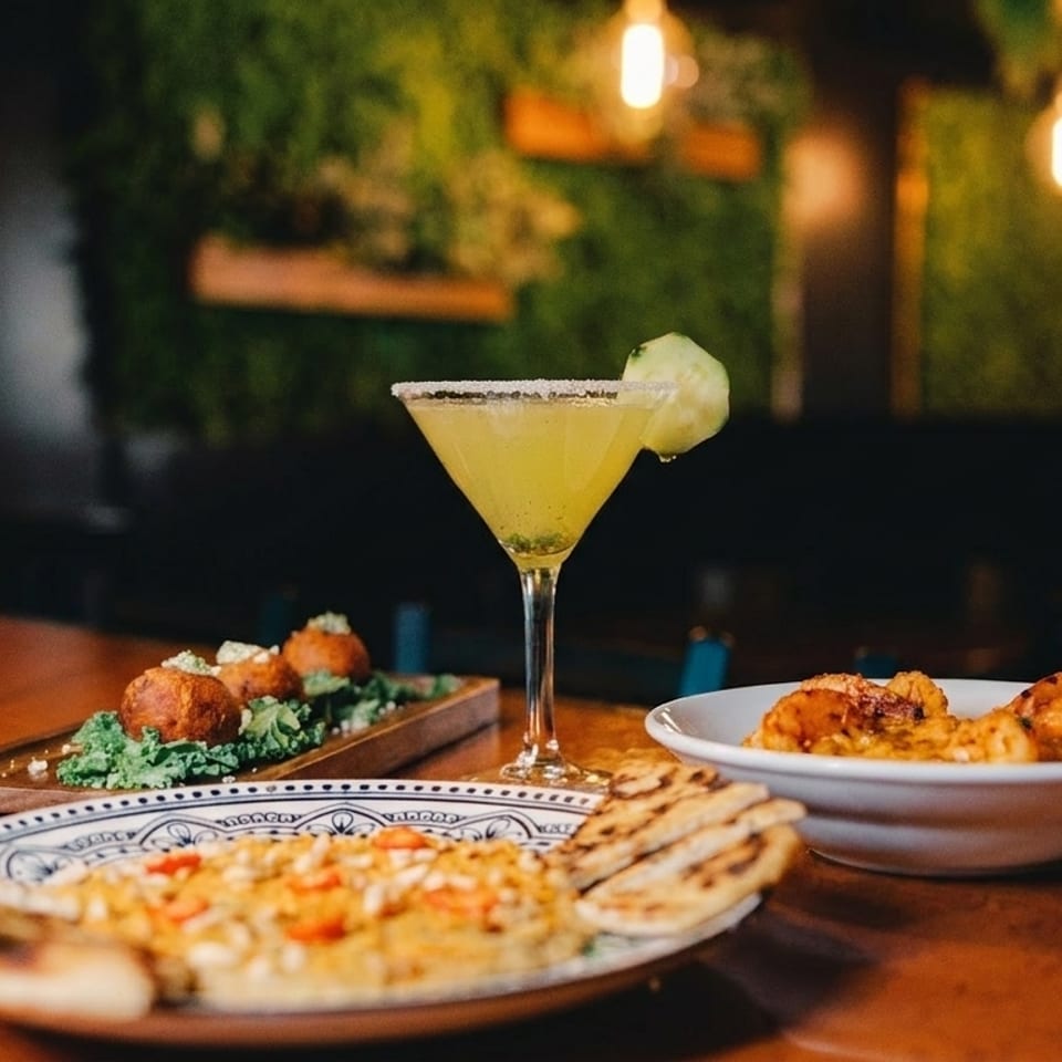 A table with a cocktail, flatbread, and two appetizers in a dimly lit restaurant.